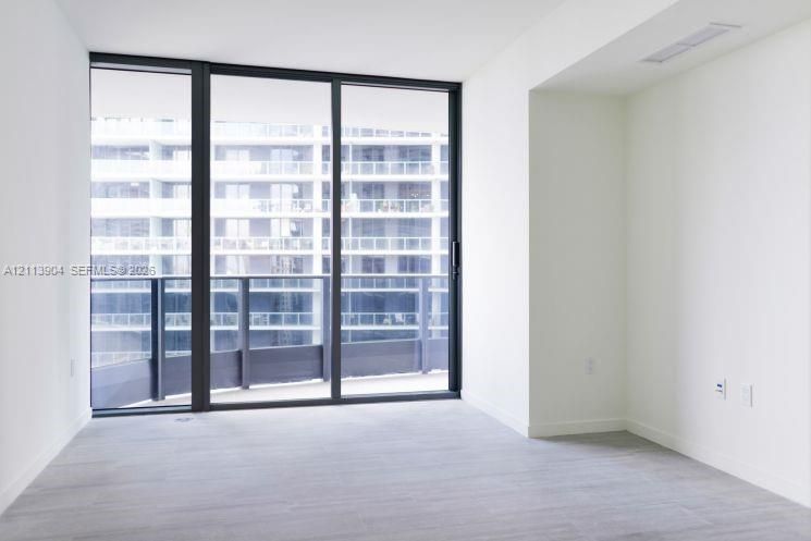 Floor-to-ceiling glass sliding doors, private balcony, wood-finish flooring, and neutral wall tones