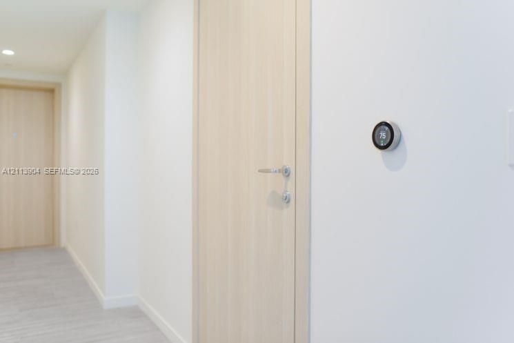 Light-toned wood-finish interior door featuring satin nickel hardware, paired with a wall-mounted smart thermostat and recessed ceiling lighting