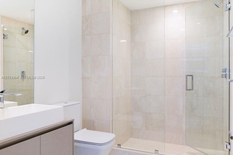 Walk-in shower with floor-to-ceiling neutral tile, frameless glass enclosure, wall-mounted shower head, and built-in vanity with a rectangular basin