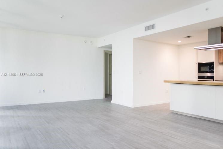 Open-concept interior featuring light wood-finish flooring, white cabinetry, a wood-topped kitchen island, and a stainless steel built-in oven and range hood