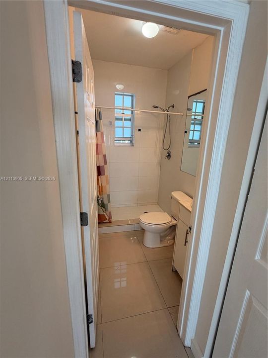 Bathroom featuring large-format tile flooring, a walk-in shower with white wall tile, a single-door vanity with integrated cabinetry, and a mounted mirror