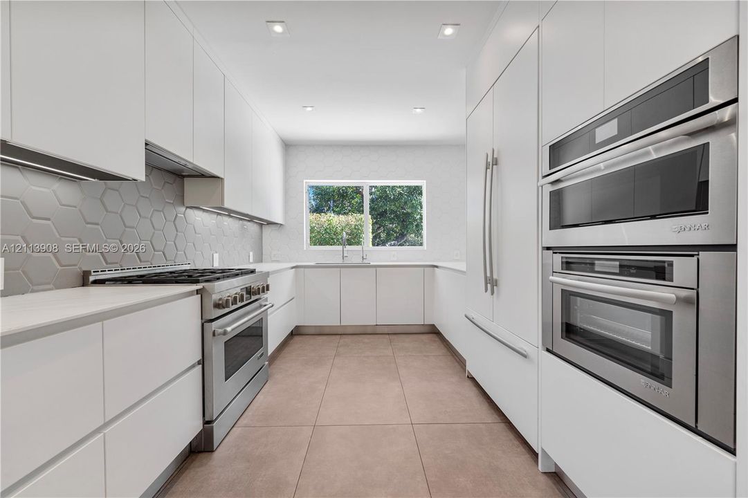 Kitchen featuring flat-panel cabinetry, stainless steel double wall ovens, a gas range, a hexagonal-pattern backsplash, and tile flooring