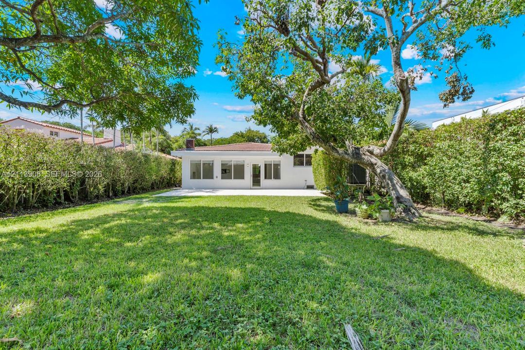 Spacious backyard featuring a manicured lawn, paved patio, mature trees, and dense perimeter hedges