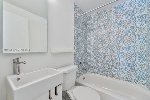 Bathroom featuring a vanity with a rectangular basin, metallic faucet, wall-mounted mirror, and a shower-tub combination accented with patterned tile surround