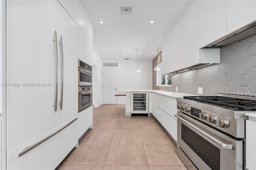 Contemporary kitchen featuring flat-panel white cabinetry, stainless steel professional-grade range, hexagonal tile backsplash, built-in wine refrigeration, and large-format tile flooring