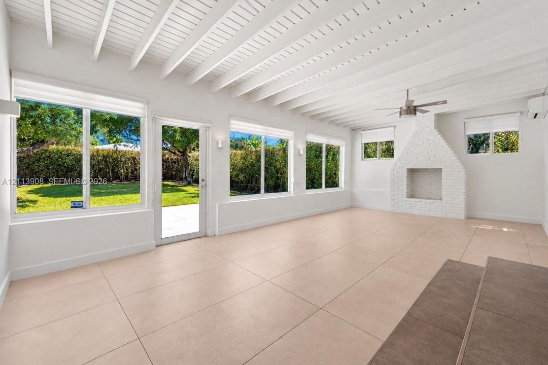 Exposed beam vaulted ceiling, white-painted brick fireplace, large-format tile flooring, oversized windows, and glass-paneled exterior door