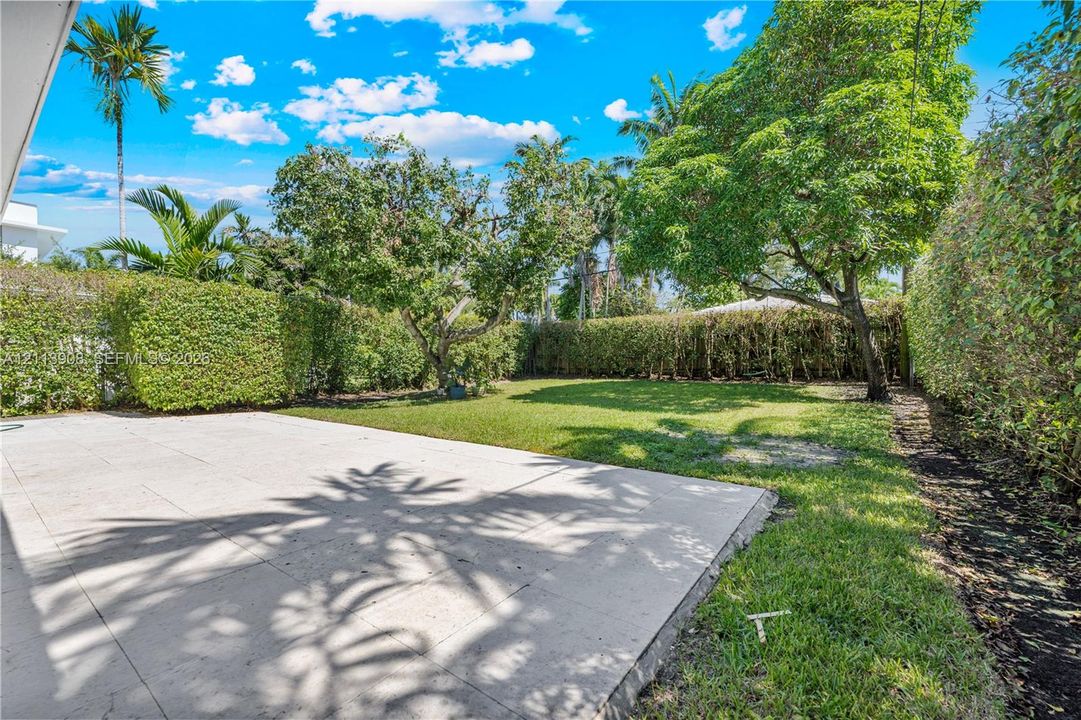 Concrete paved patio featuring a grass lawn, mature trees, and perimeter shrubbery