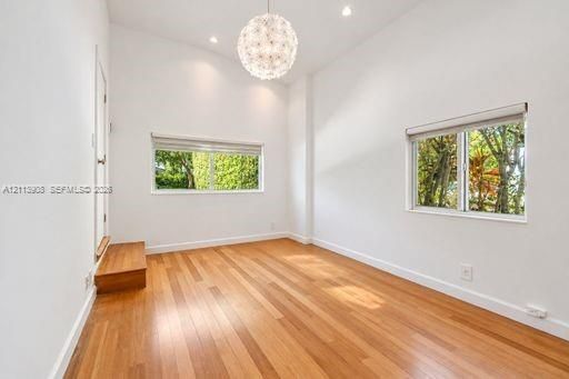 High-ceilinged room featuring wood-finish flooring, recessed lighting, a modern spherical pendant fixture, and large windows