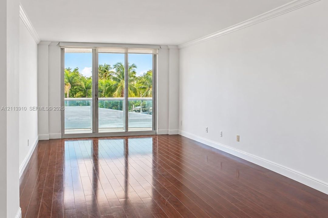 Open-concept interior featuring wood-finish flooring, crown molding, and floor-to-ceiling glass sliding doors leading to a balcony with a glass railing