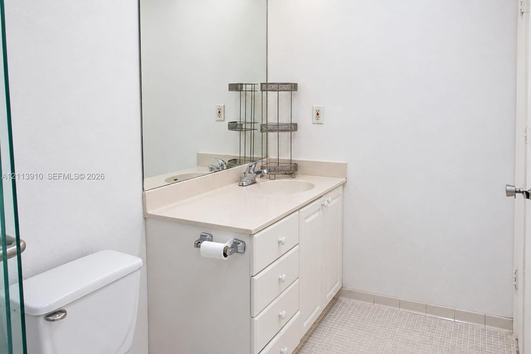 Vanity featuring a solid-surface countertop with an integrated basin, white cabinetry, a large wall-mounted mirror, and tile flooring