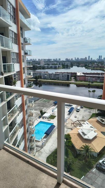 Private balcony featuring glass railings, overlooking a swimming pool, waterfront, and cityscape skyline
