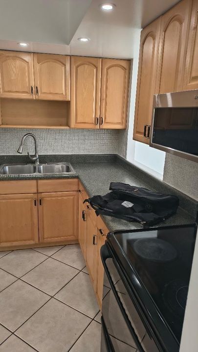 Kitchen featuring light-finish wood cabinetry, solid-surface countertops, mosaic tile backsplash, double-basin stainless steel sink with pull-down faucet, and ceramic tile flooring