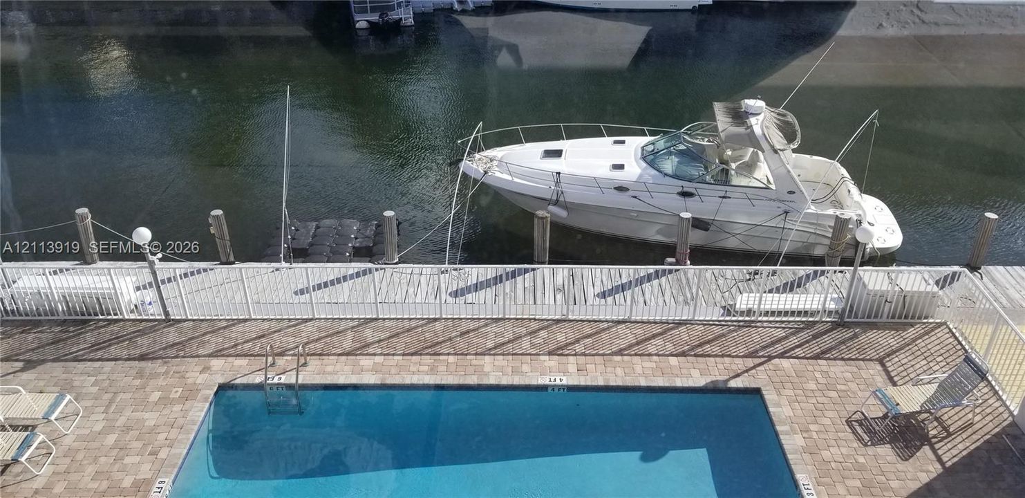 Dock space available! Waterfront deck featuring an in-ground pool, stone paver surround, white metal safety railing, and a private bulkhead with boat slip