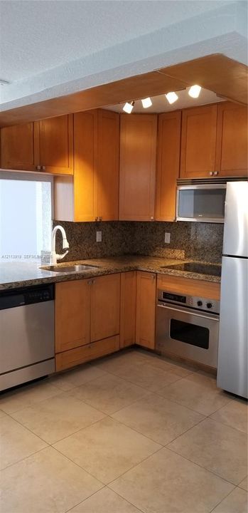 Kitchen featuring flat-panel wood cabinetry, stone countertops, stainless steel appliances, a high-arc faucet, and tiled flooring