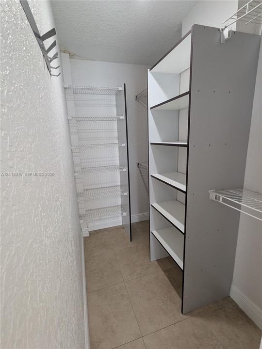 Storage space featuring built-in vertical shelving units and wall-mounted wire rack shelving systems with tile flooring