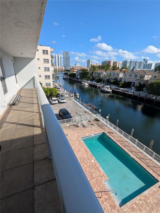 Private balcony with tile flooring, overlooking an in-ground swimming pool, brick-paved pool deck, and a deep-water canal