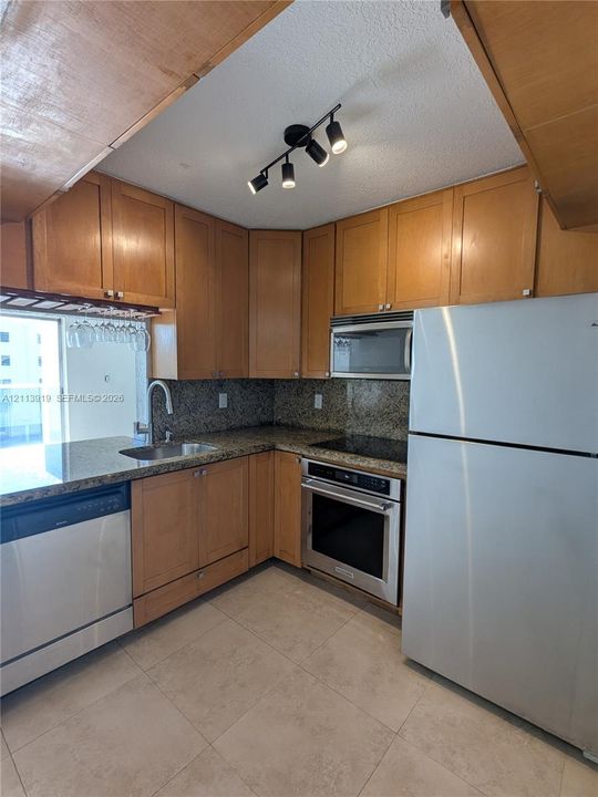 Kitchen featuring natural finish cabinetry, stone countertops, stainless steel appliances, tile flooring, and multi-directional track lighting