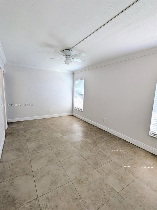 Interior room featuring large-format stone-finish floor tile, crown molding, multi-blade ceiling fan, and two windows with horizontal blinds