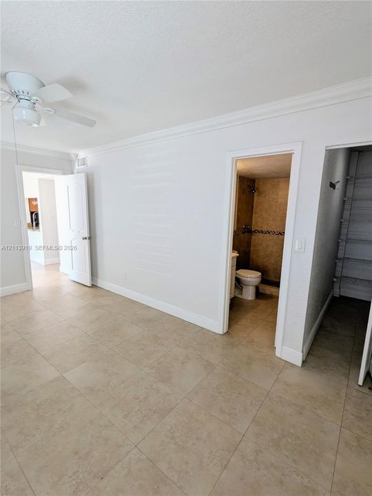 Room featuring large-format neutral tile flooring, crown molding, and a white ceiling fan with integrated lighting