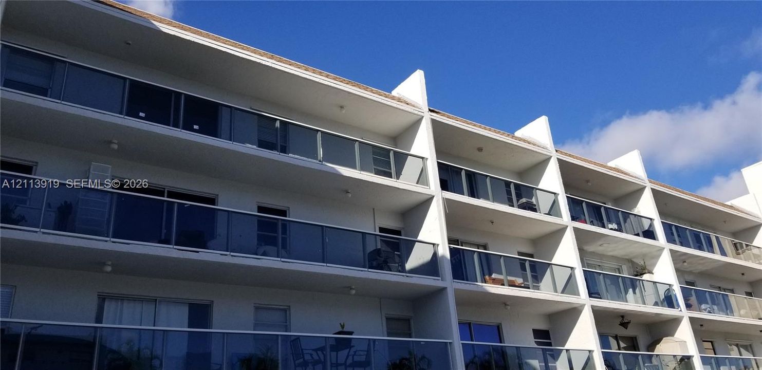 Multi-story residential exterior featuring glass-panel balcony railings and recessed private balcony spaces