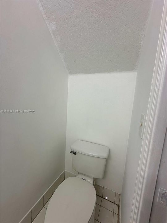 White toilet with an elongated bowl, tile flooring, and angled ceiling