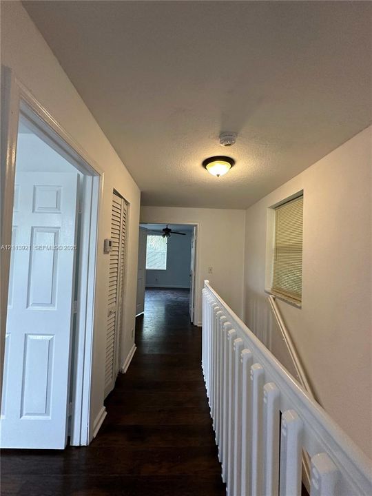 Hallway featuring wood-finish flooring, white paneled doors, louvered closet doors, and a white baluster railing