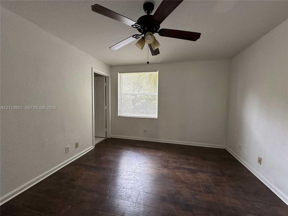 Room featuring wood-finish flooring, a central ceiling fan with integrated lighting, and a single-pane window
