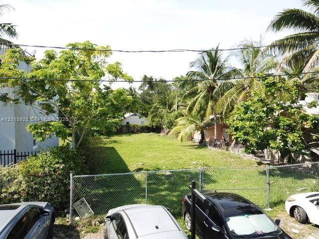 Open lot featuring a grass lawn, chain-link perimeter fencing, and mature palm and hardwood trees