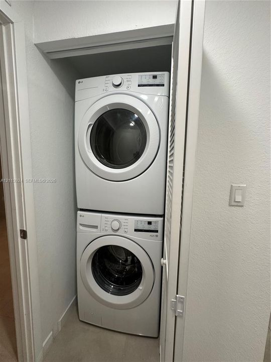 Stacked washer and dryer unit housed within a dedicated closet featuring a louvered door