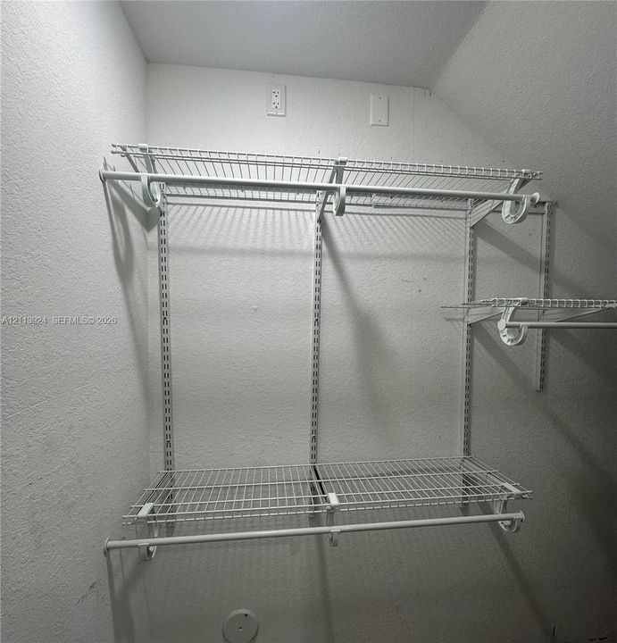 Walk-in storage space featuring adjustable white wire shelving and dual hanging rods