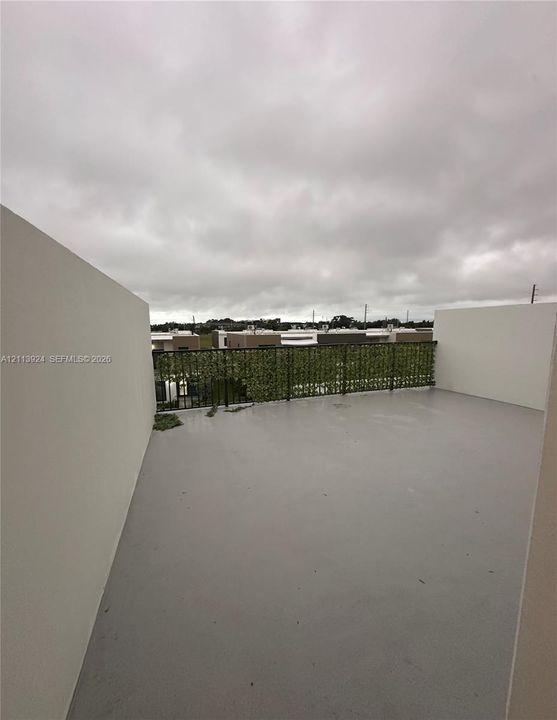 Rooftop terrace featuring smooth concrete flooring, solid privacy walls, and a metal railing with integrated greenery