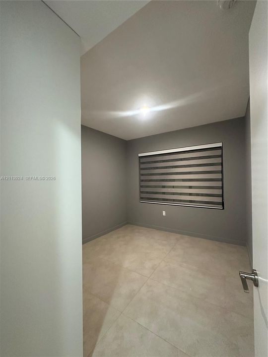 Neutral-toned interior space featuring large-format tile flooring, grey wall finish, and a window equipped with horizontal zebra-style blinds