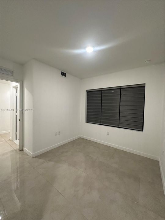 Neutral interior featuring large-format ceramic tile flooring, solid white walls, and a recessed window with installed horizontal dual-shade blinds
