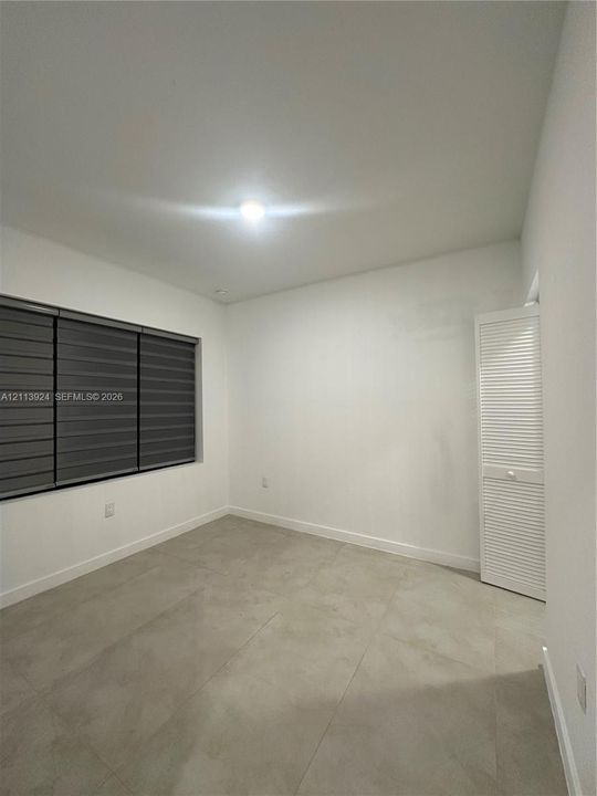 Room featuring large-format tile flooring, white walls, louvered closet doors, and multi-band window shades