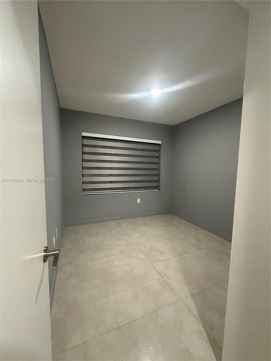 Neutral-toned interior room featuring large-format tile flooring, gray walls, and a window equipped with banded roller shades