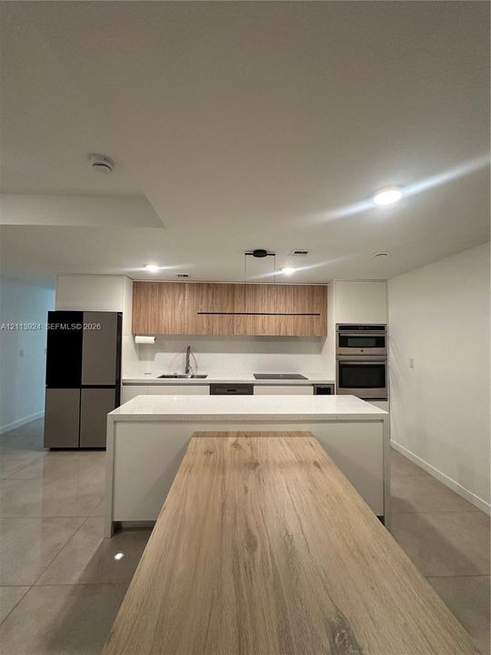 Kitchen featuring dual-tone cabinetry, wood-finish upper cabinets, a waterfall-edge kitchen island, integrated appliances, and large-format tile flooring
