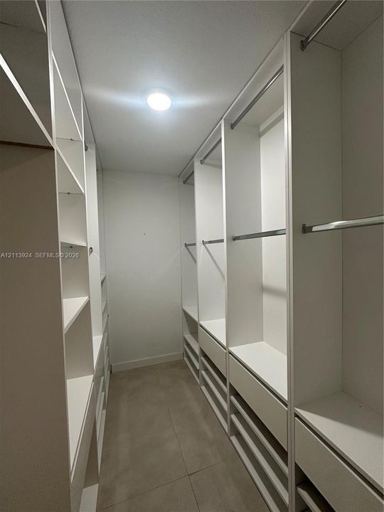 Walk-in closet featuring white custom built-in cabinetry, tiered shelving, integrated clothing rods, and tile flooring