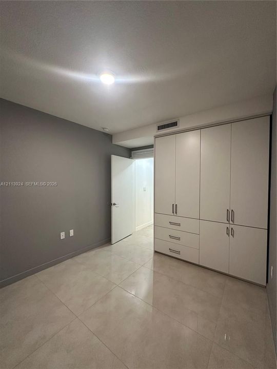 Room featuring large-format tile flooring, built-in floor-to-ceiling white cabinetry with integrated drawers, and a ceiling-mounted light fixture