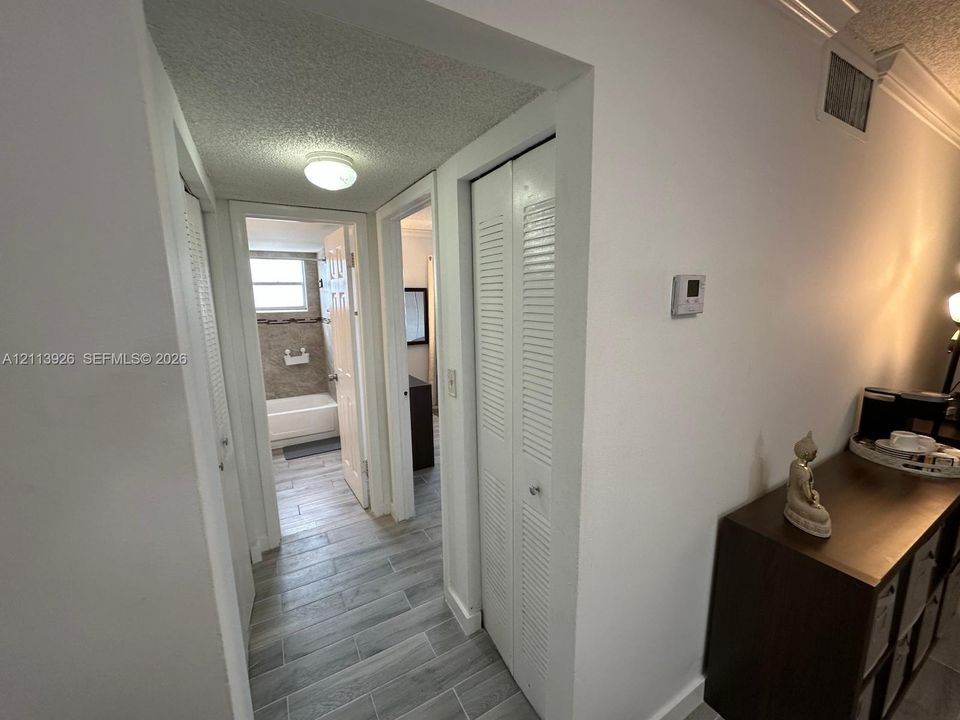 Hallway featuring wood-finish tile flooring, multiple louvered-door closets, and crown molding