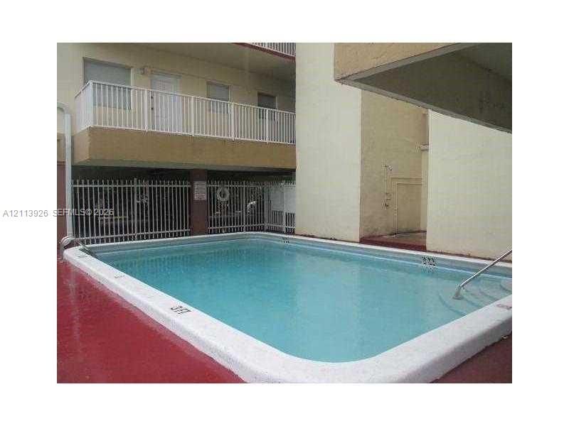 Swimming pool featuring a concrete deck, integrated steps, and metal handrails, bordered by a white perimeter fence and multi-level structure