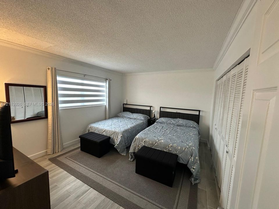 Bedroom featuring wood-finish tile flooring, dual louvered-style closet doors, a wide window with integrated horizontal blinds, and crown molding