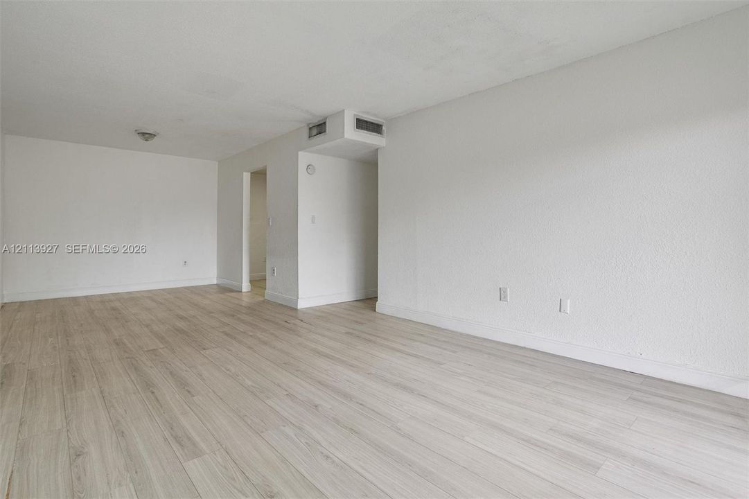 Open-concept interior featuring light-toned wood-finish flooring, smooth-textured walls, and a flush-mount ceiling light fixture