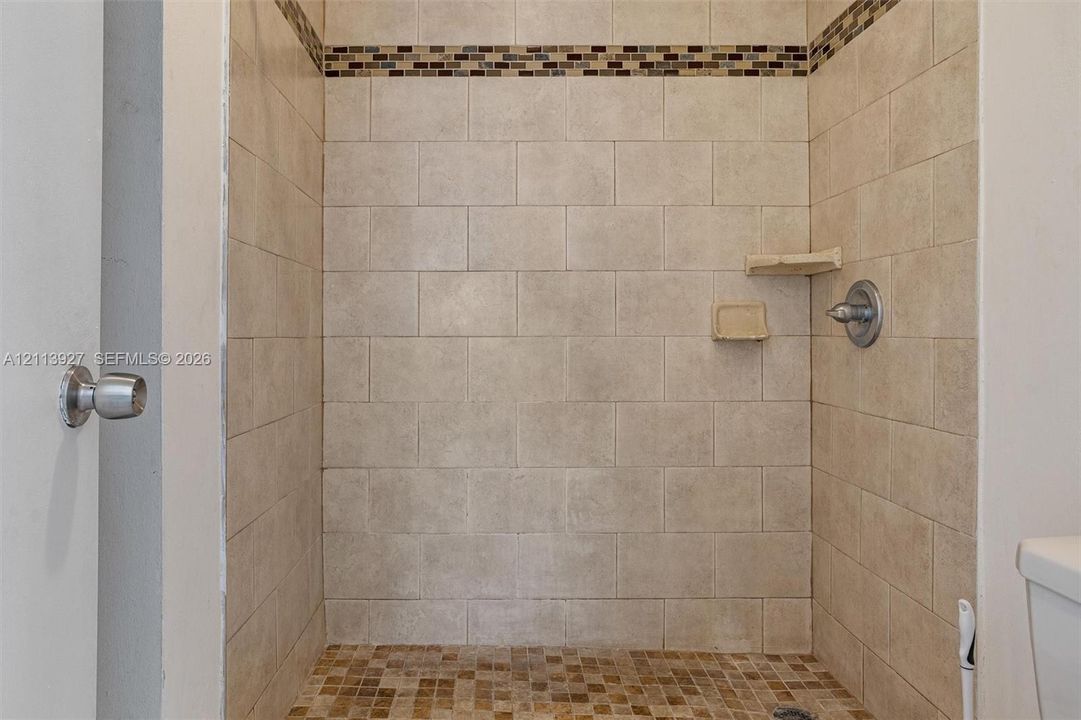 Walk-in shower featuring neutral rectangular wall tile, mosaic tile accent border, integrated corner shelving, and brushed nickel hardware