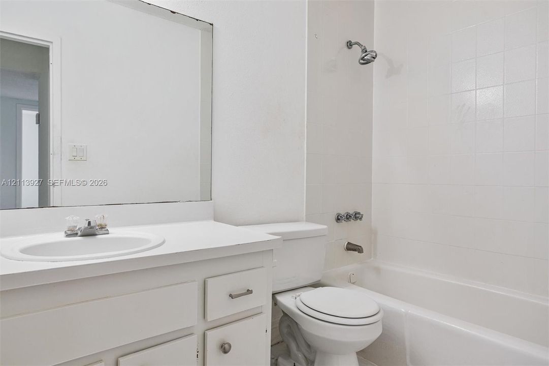 Bathroom featuring a white vanity cabinet with a integrated sink, a large wall-mounted mirror, a porcelain toilet, and a tiled shower-tub combination with chrome fixtures