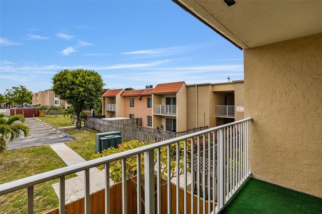 Covered balcony featuring white metal railings and green floor surfacing