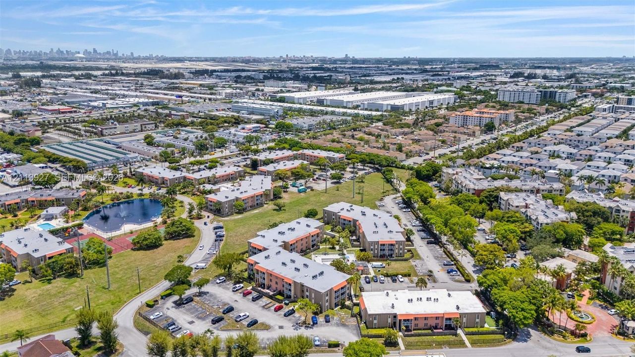 Aerial perspective featuring multi-story residential buildings, surface parking areas, on-site pond, and landscaped green space
