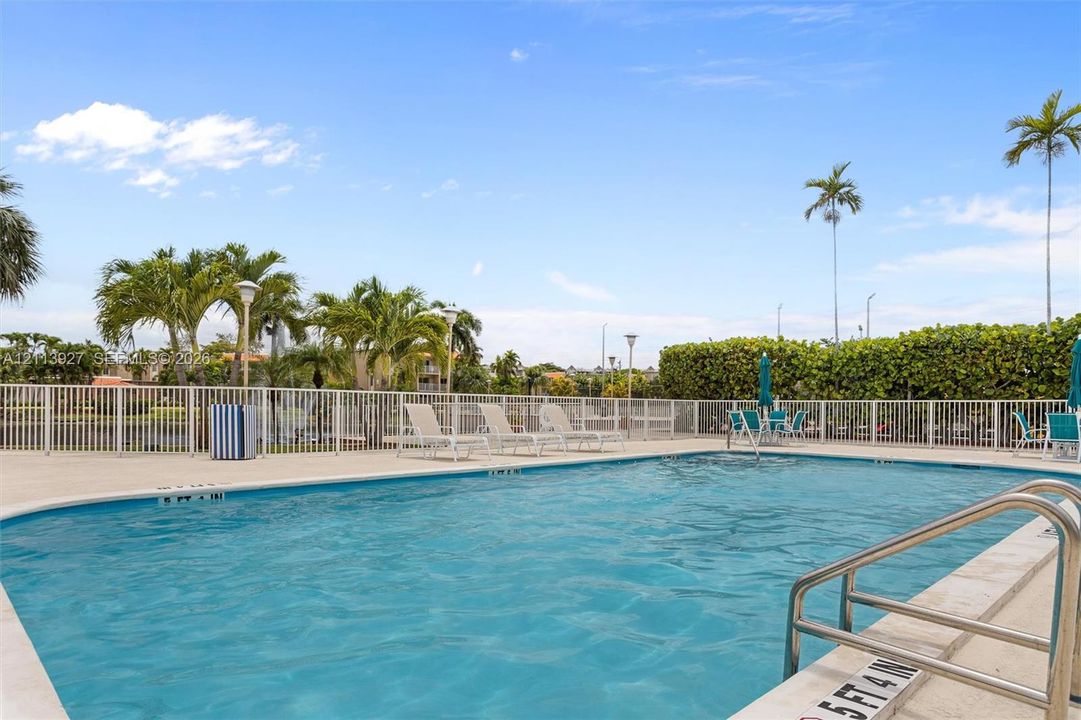 Outdoor swimming pool featuring a concrete deck, metal perimeter fencing, and stainless steel ladder rails