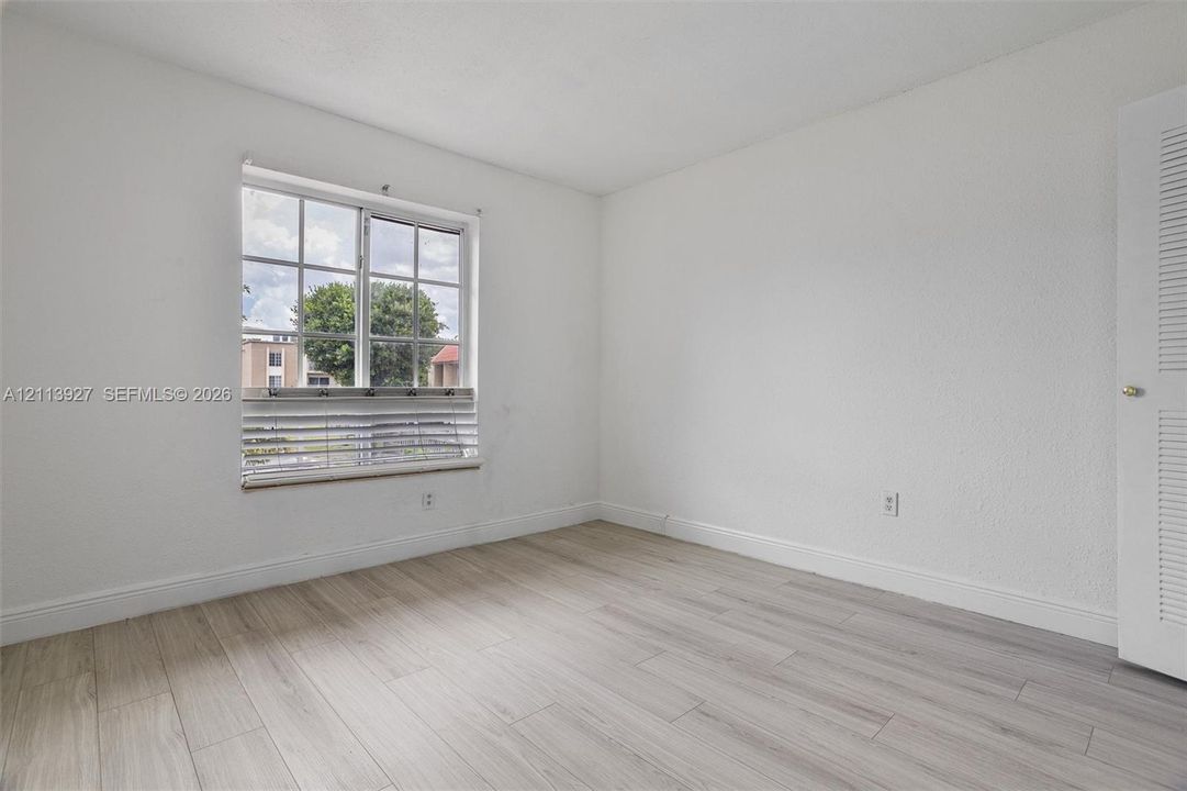 Neutral interior featuring light wood-finish flooring, white walls, and a multi-pane window with louvered blinds