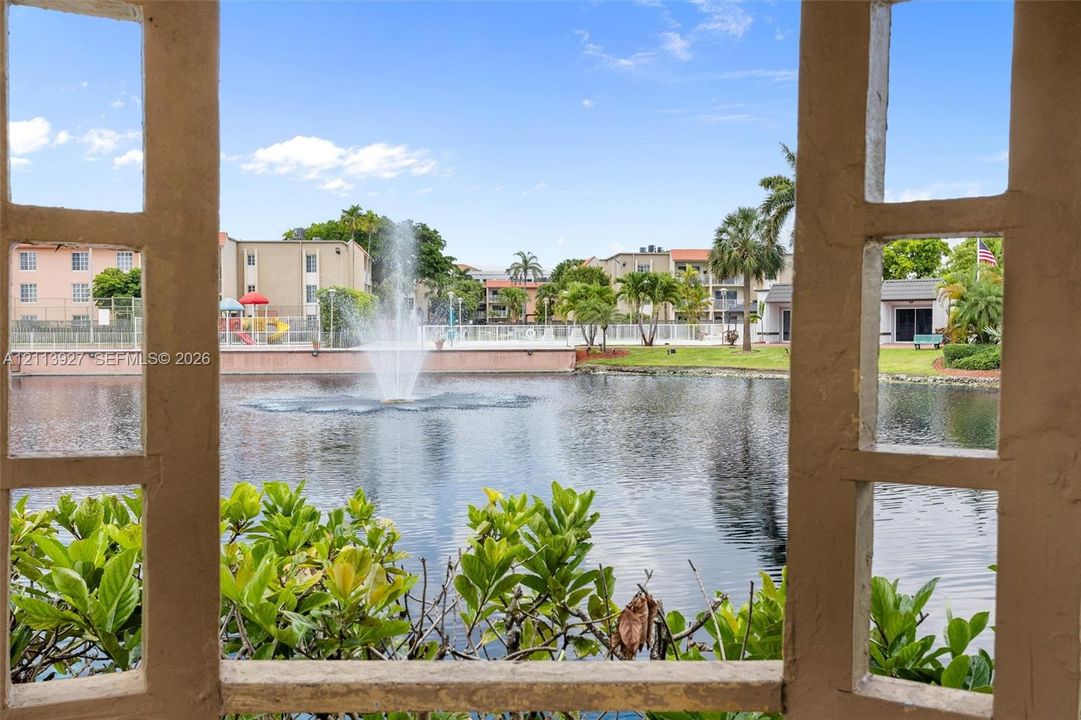 Stucco-framed gazebo structure overlooking a central pond featuring a built-in fountain, perimeter landscaping, and established palm trees