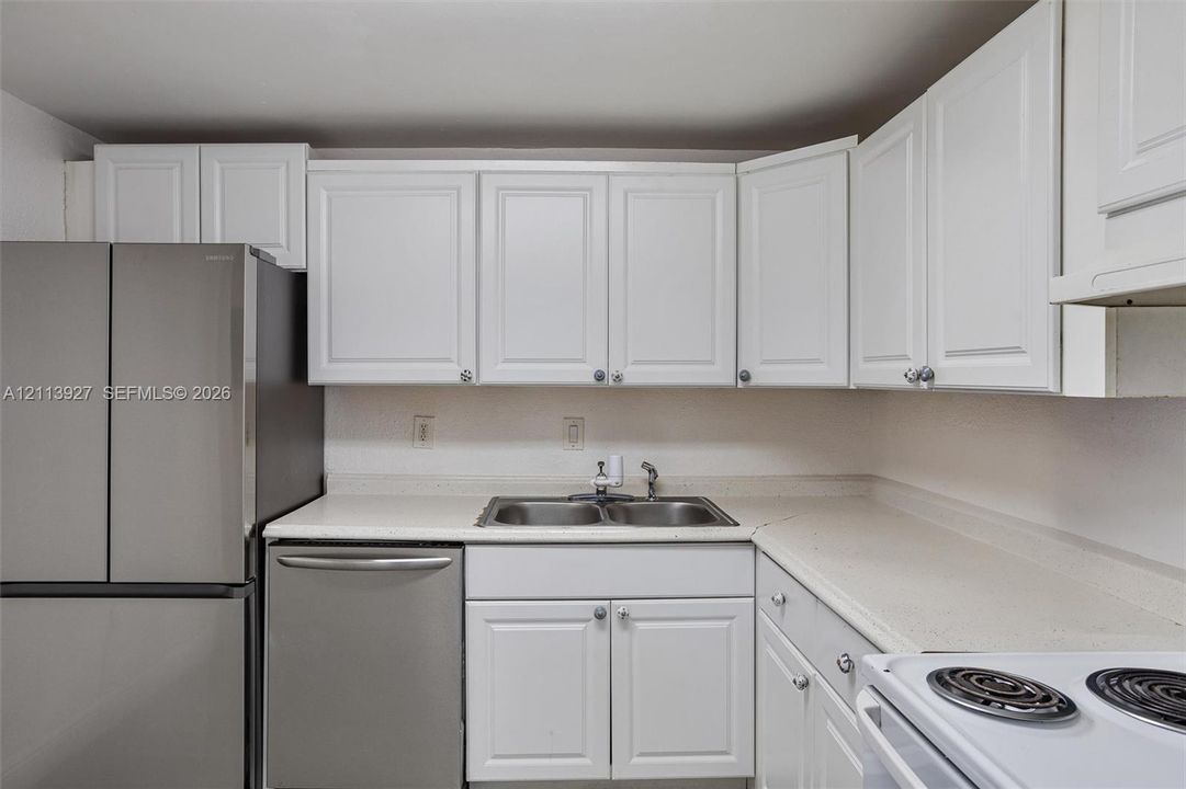 Kitchen featuring white shaker-style cabinetry, solid-surface countertops, dual-basin stainless steel sink, and stainless steel appliances